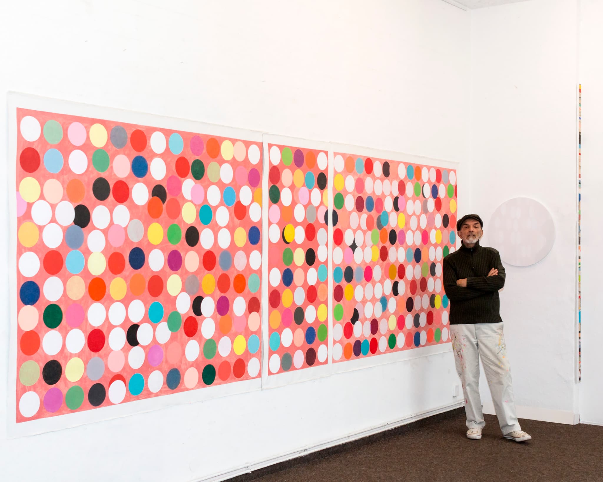 Sam Grigorian standing in his Berlin studio in front of the Happiness series, a large triptych of coloured circles on a red ground.